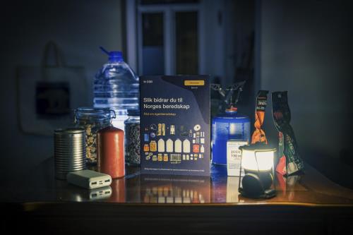 Bildet viser brosjyre for Egenberedskapsuka og diverse mat- og drikkevarer på et bord i mørke omgivelser.