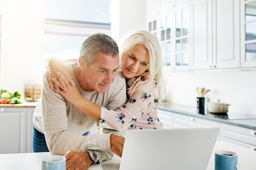 En mann og en kvinne i 50-årene ser på en pc, mens kvinnen holder rundt mannen.