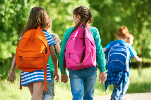 Tre barn som er på vei til skolen med skolesekk på ryggen.