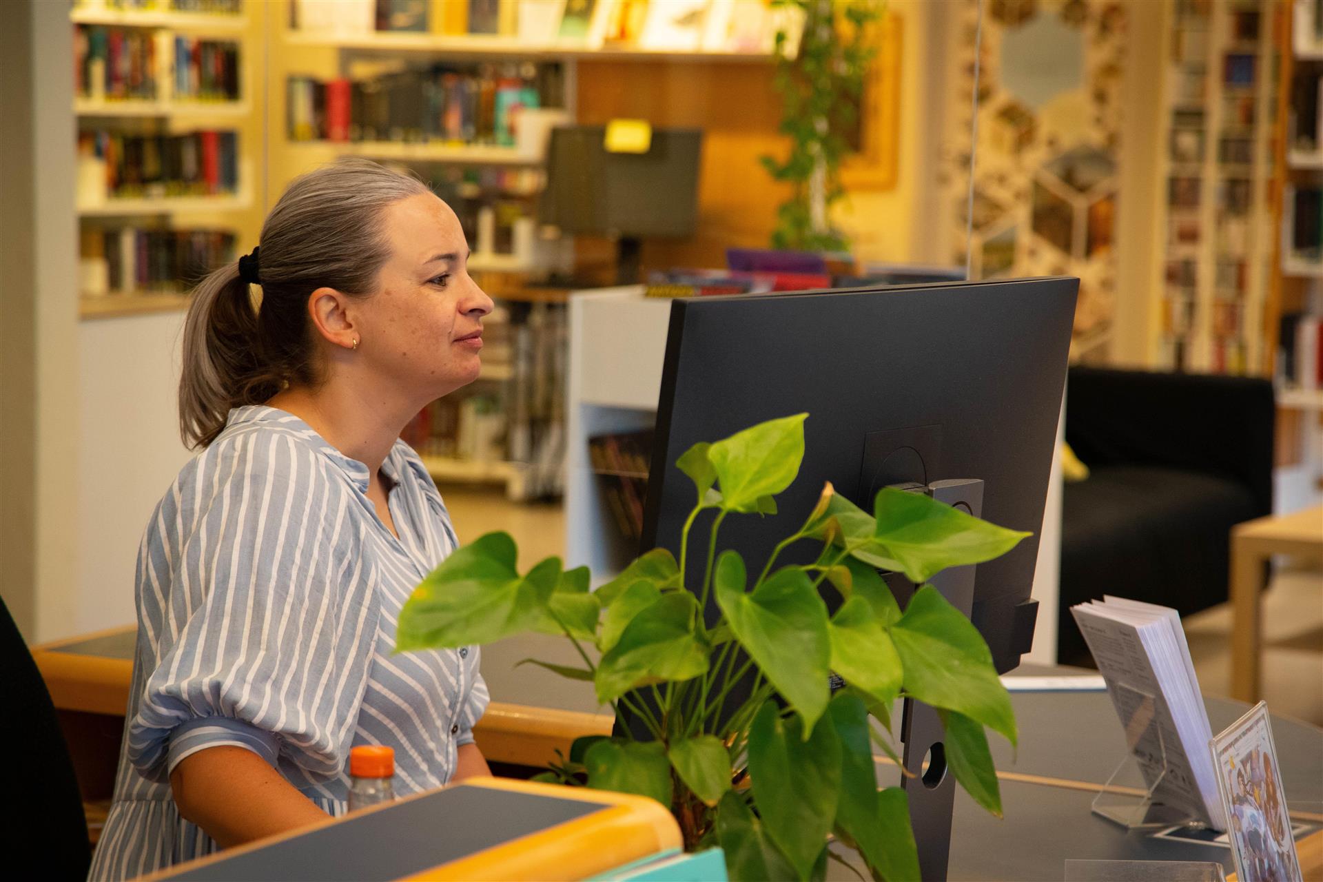 Bibliotekar sitter foran skranken og jobber på datamaskinen.